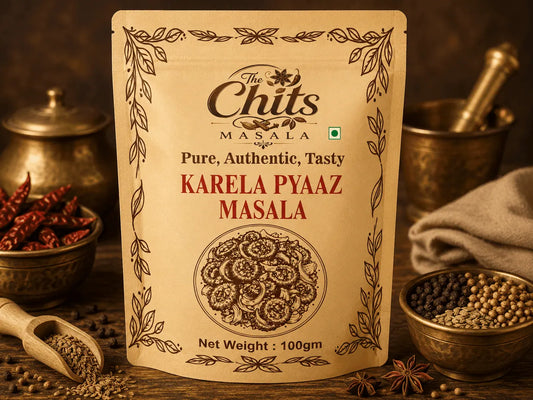 A 100g stand-up pouch of 'The Chits Masala Karela Pyaaz Masala' spice blend, displayed on a rustic wooden table surrounded by whole spices, dried red chilies, and brass utensils.
