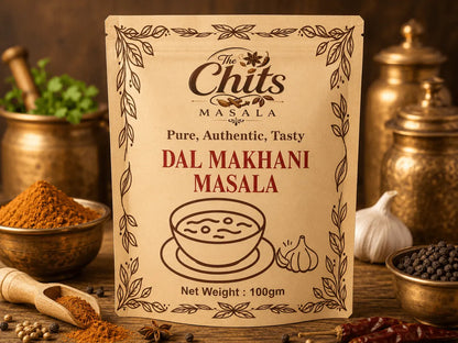 A package of Dal Makhani Masala by The Chits Masala stands upright on a rustic wooden surface, surrounded by spices, brass containers, garlic, and dried red chilies in a warm, appetizing setting.