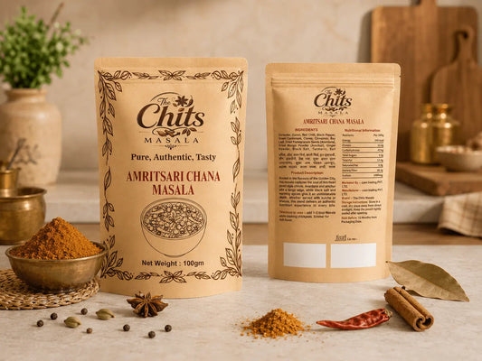 Two stand-up pouches of The Chit's Masala Amritsari Chana Masala spice mix displayed on a kitchen counter with whole spices, dried red chilies, and a bay leaf.