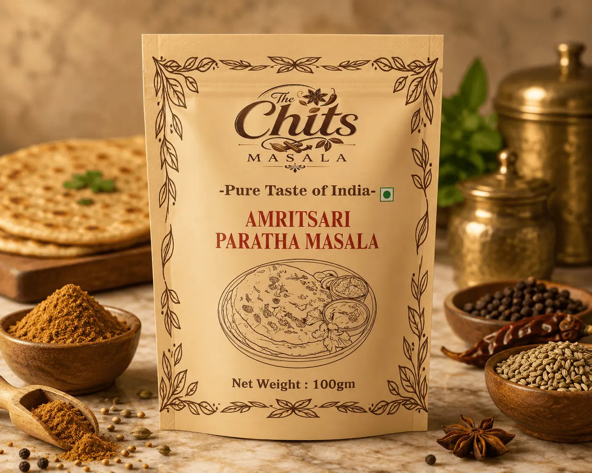 A 100g stand-up pouch of The Chits Masala Amritsari Paratha Masala centered on a rustic tabletop, surrounded by bowls of whole spices, a wooden spoon with ground spice, flatbread, and brass containers in a warm, styled setting.