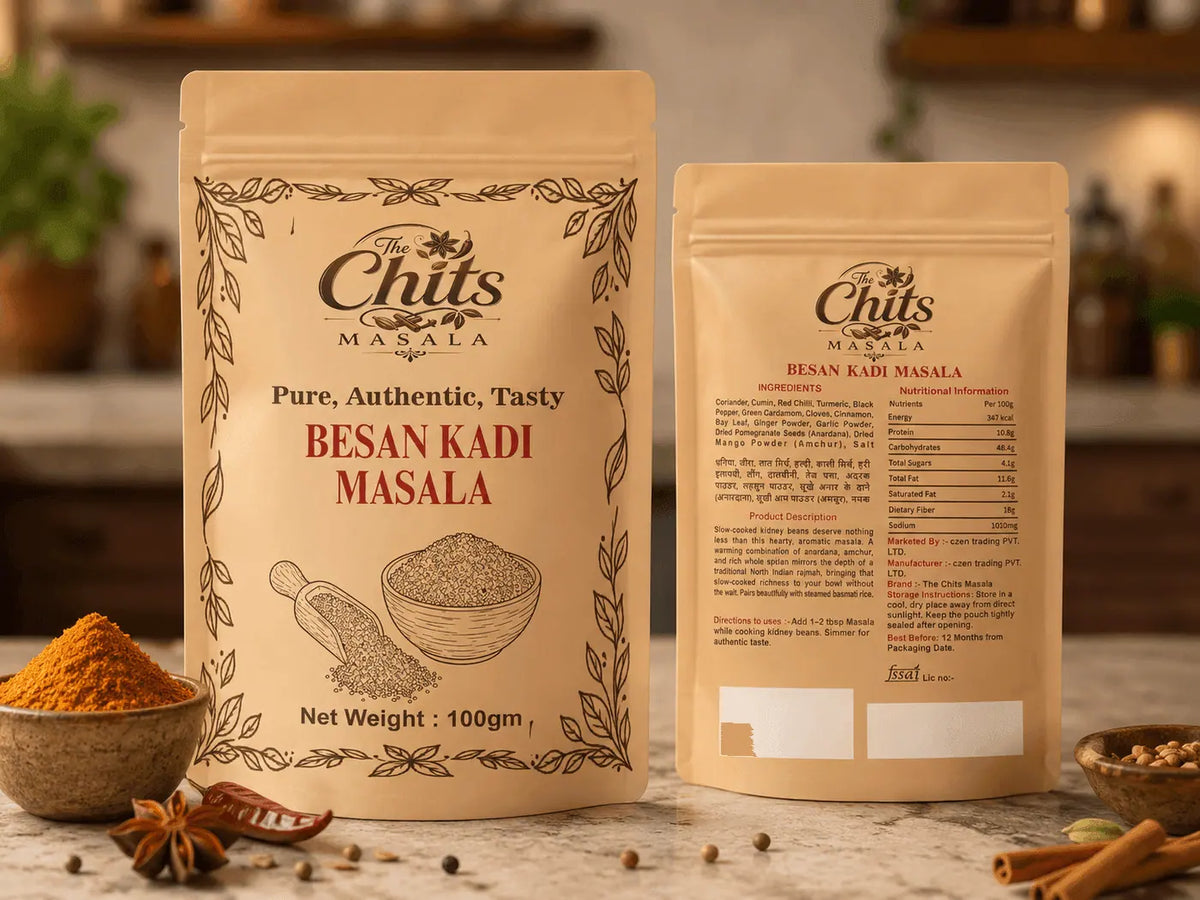 Two stand-up pouches of The Chits Masala Besan Kadi Masala shown on a countertop, with bowls of ground spice and whole spices arranged around them in a warm kitchen setting.