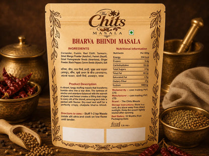 The Chit Masala Bharva Bindi Masala seasoning packet shown against a warm, dark background with bowls of whole spices and red chili powder. The packet is beige with brown decorative borders and text detailing the ingredients and nutritional information.