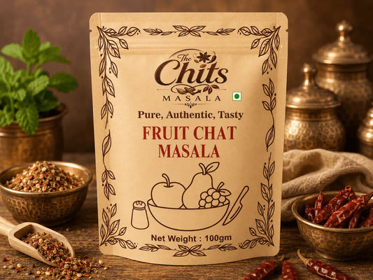 A stand-up pouch of The Chits Masala Fruit Chat Masala centered on a rustic wooden surface, surrounded by bowls of spices, dried red chilies, and a small plant in the background.