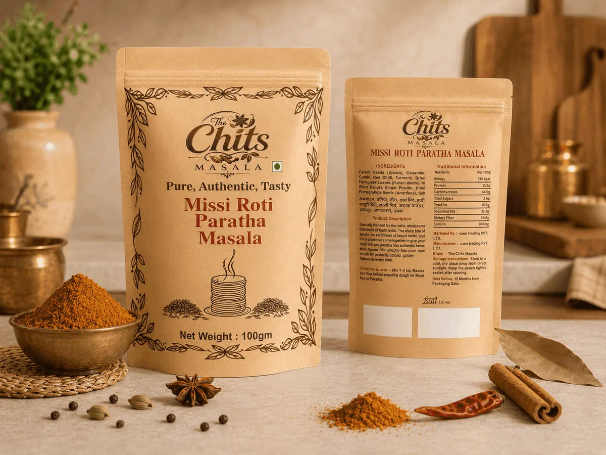 Two stand-up pouches of Chits Masala Missi Roti Paratha Masala displayed on a kitchen counter with spices, dried chilies, cinnamon sticks, and a leaf, with a blurred kitchen background.
