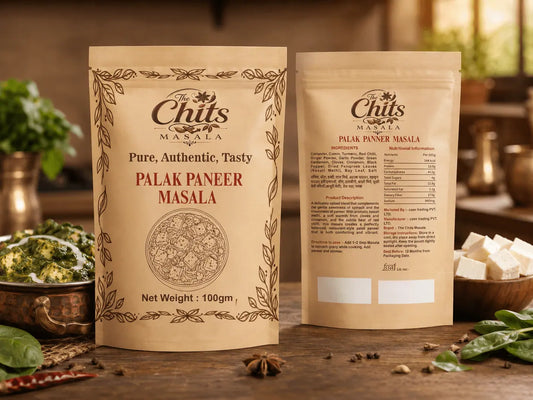 Two stand-up pouches of Palak Paneer Masala by The Chit's Masala displayed on a rustic wooden table with ingredients like spinach, onions, and paneer cubes in a warm kitchen setting.