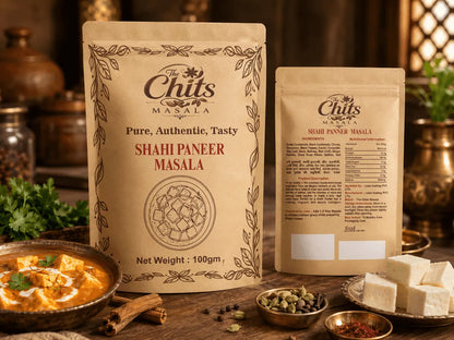 Two stand-up pouches of The Chits Masala seasoning blends displayed on a rustic wooden table with food props including paneer cubes, a bowl of chutney, and spices. One pouch is labeled 'Shahi Paneer Masala' and the other 'Slurpee Paneer Masala'.