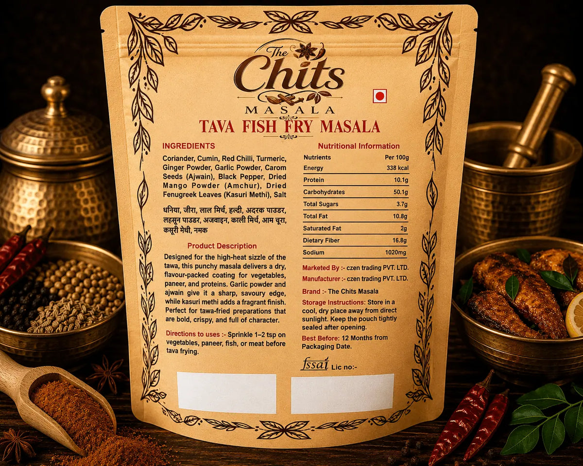 A stand-up pouch of Tava Fish Fry Masala by The Chits Masala, displayed on a wooden surface with spices and kitchen props around it. The front of the package is tan with black text and decorative border illustrations, and the back shows ingredients and nutritional information in English and Hindi.